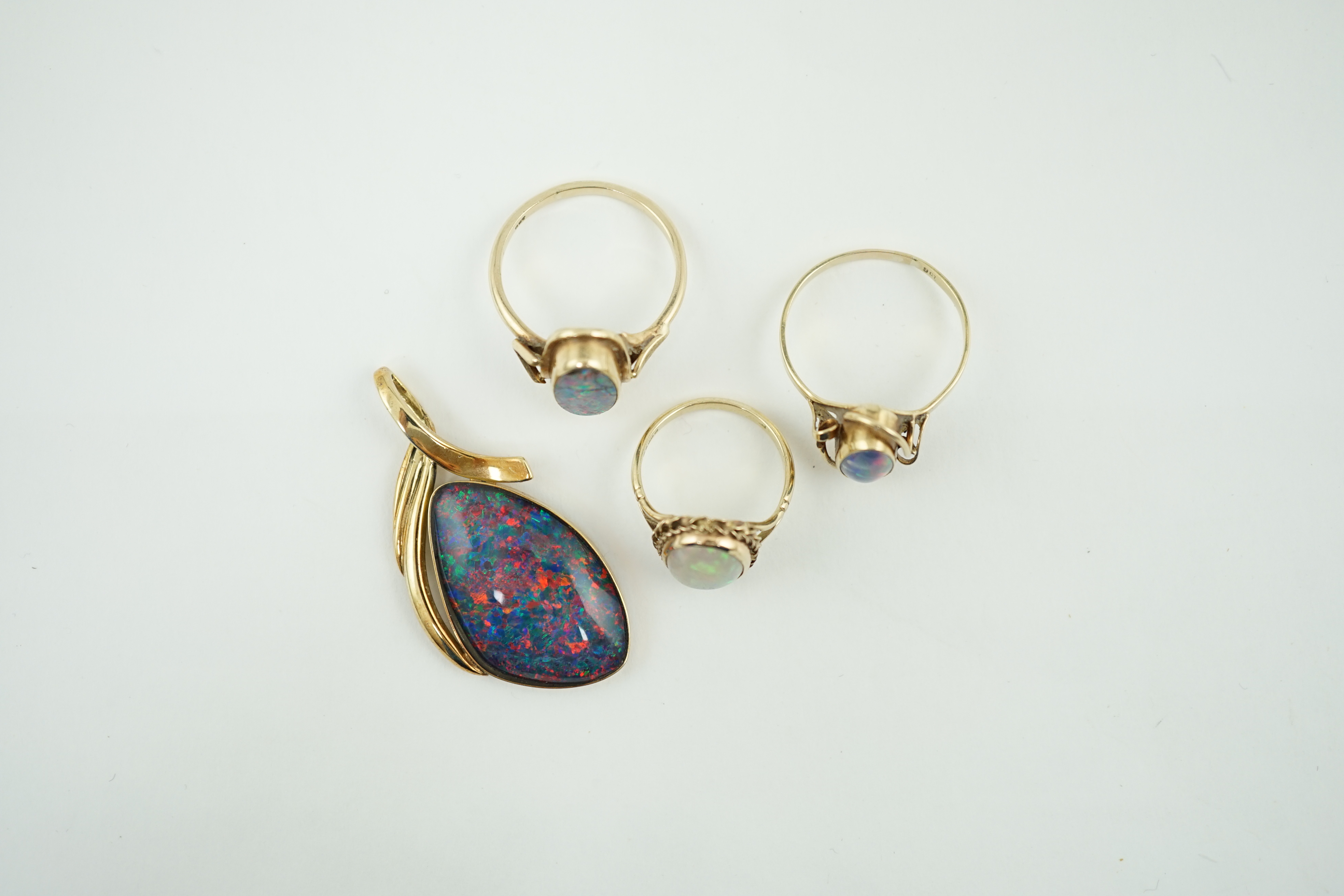 A modern 14k gold and black opal set pendant, 44mm, together with three assorted 9ct gold and single stone cabochon opal set rings